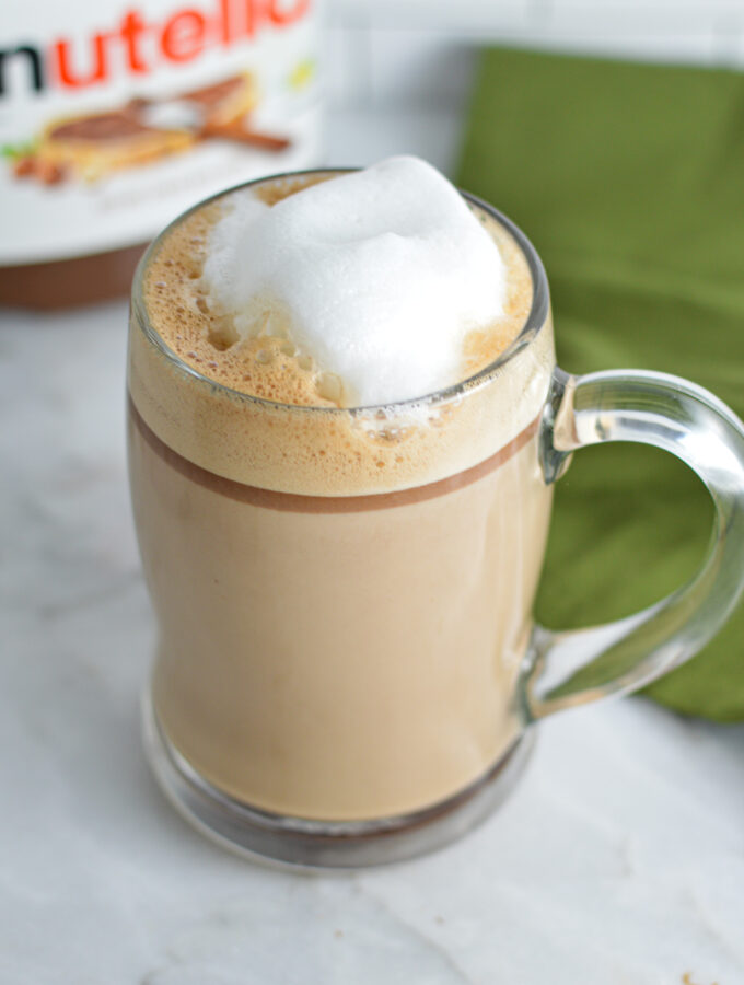 Nutella Latte with frothed milk on top and a jar of Nutella in the background.