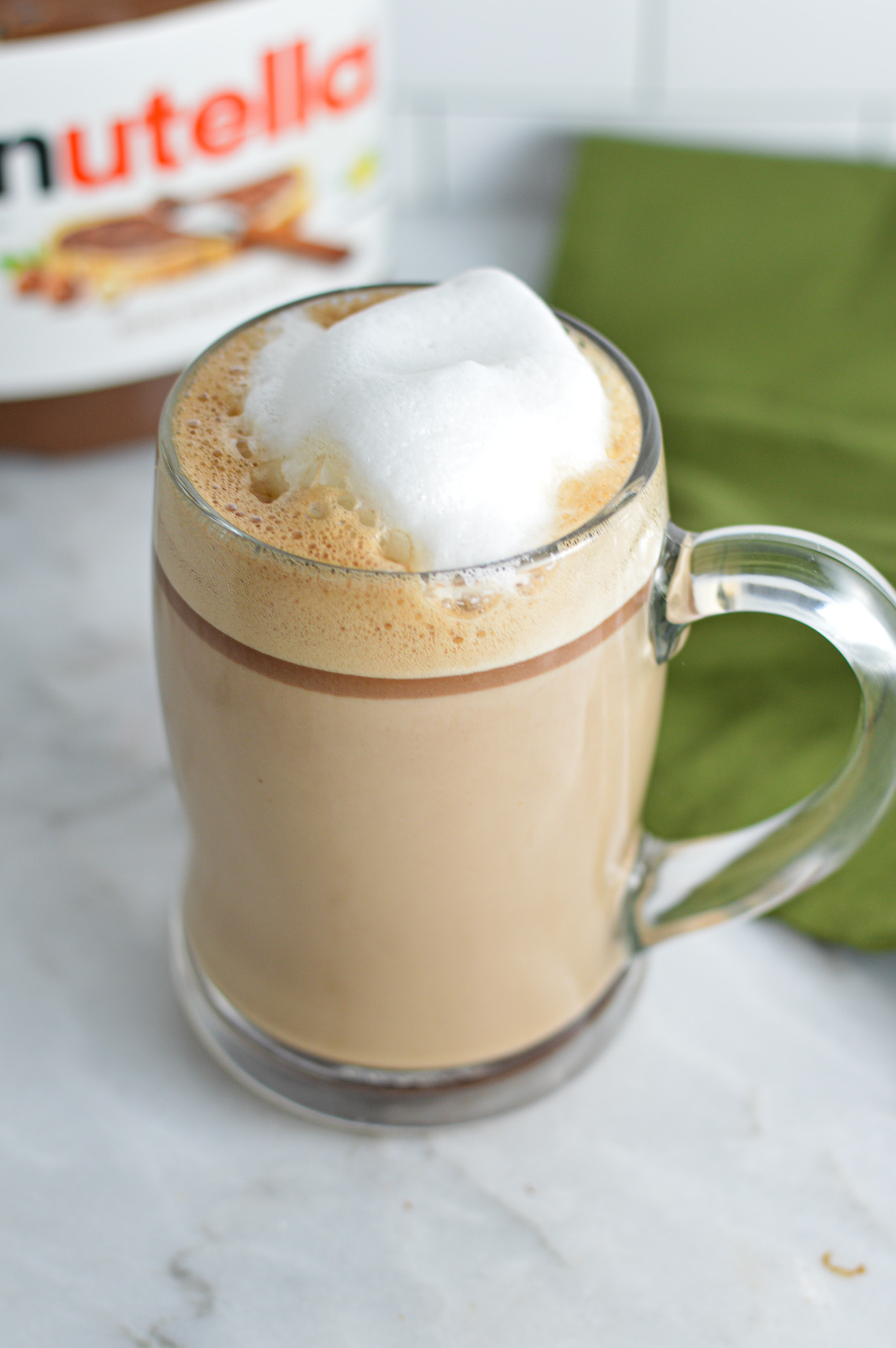 Nutella Latte with frothed milk on top and a jar of Nutella in the background.