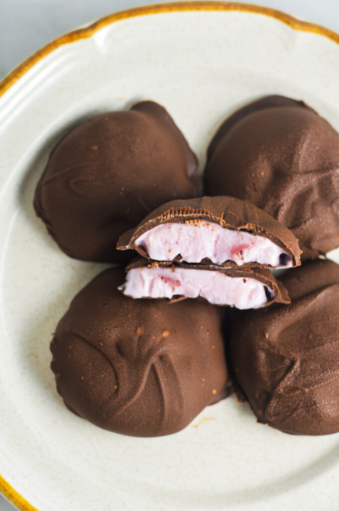 A closeup of 3 Ingredient Chocolate Yogurt Clusters arranged on a small plate. The creamy yogurt filling is surrounded by a hard chocolate shell.