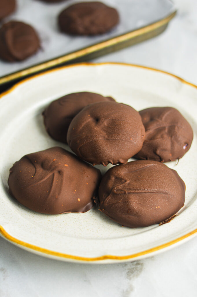 3 Ingredient Chocolate Yogurt Clusters arranged on a small white plate with more chocolate clusters on a baking sheet.