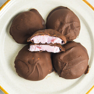 3 Ingredient Chocolate Yogurt Clusters on a ceramic plate with center chocolate bite cut in half. The berry yogurt filling is surrounded by melted rich chocolate with a slightly uneven, rustic appearance.