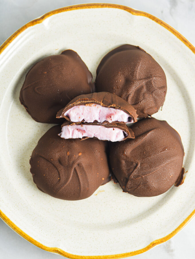 3 Ingredient Chocolate Yogurt Clusters on a ceramic plate with center chocolate bite cut in half. The berry yogurt filling is surrounded by melted rich chocolate with a slightly uneven, rustic appearance.