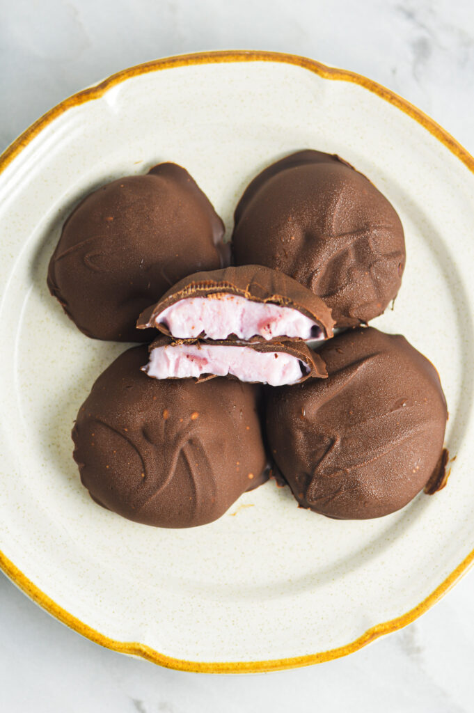 3 Ingredient Chocolate Yogurt Clusters on a ceramic plate with center chocolate bite cut in half. The berry yogurt filling is surrounded by melted rich chocolate with a slightly uneven, rustic appearance.