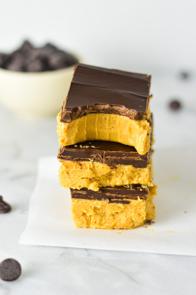 A stack of Buckeye Bars on a sheet of parchment paper with a bite taken out of the top showing the rich and fudgy texture.