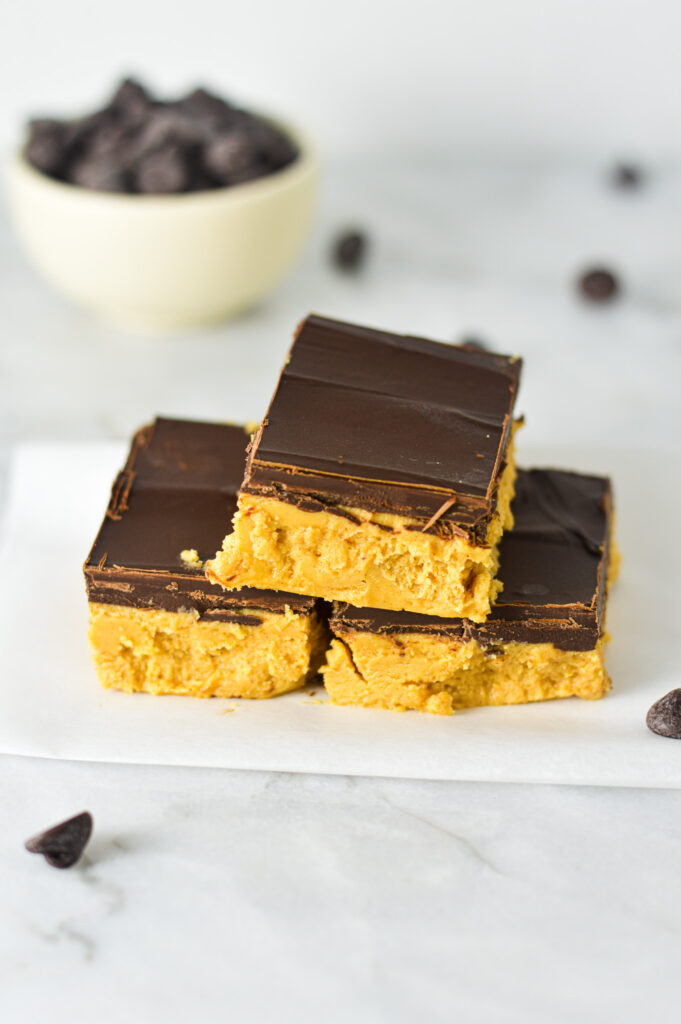 Some Buckeye Bars neatly arranged on some wax paper with semi-sweet chocolate chips in a small bowl in the background.