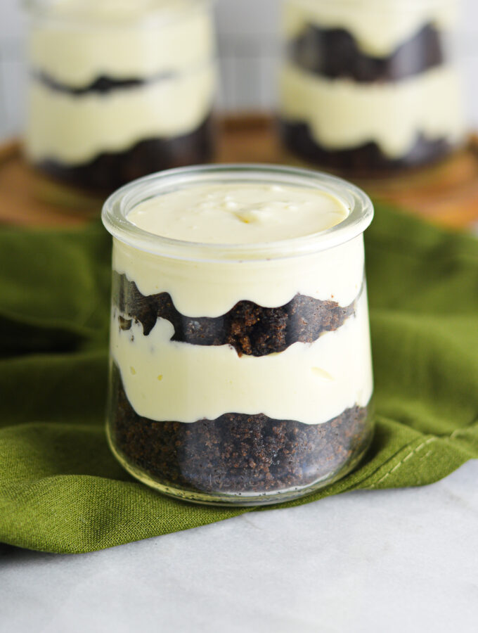 Three Chocolate Cake Cheesecake Cups in small glass containers. Each individual dessert is layered with dark brown chocolate cake and no bake cheesecake.