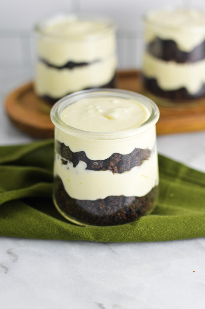 Cheesecake filling and dark chocolate cake are layered in three small glass jars.