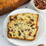 Two slices of Cranberry Pecan Banana Bread with pecans in the background.