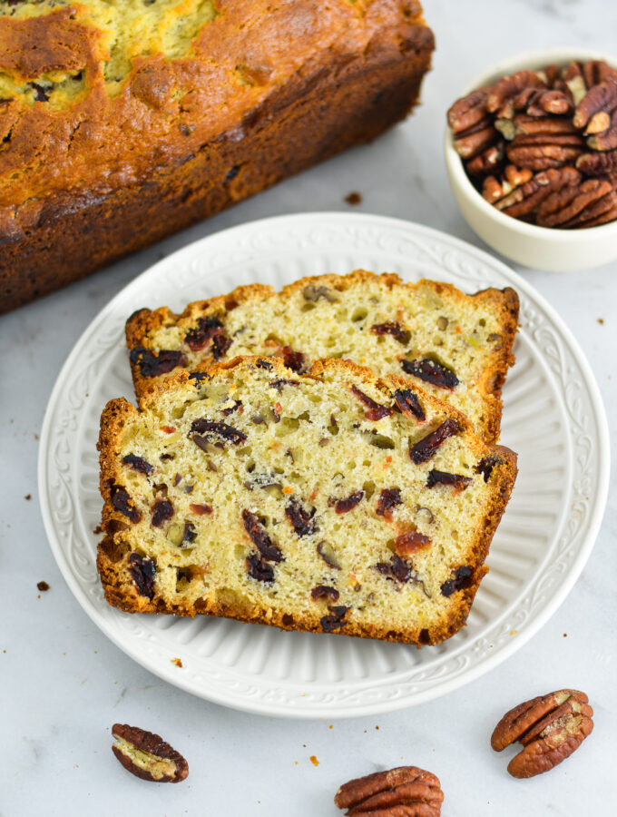 Two slices of Cranberry Pecan Banana Bread with pecans in the background.