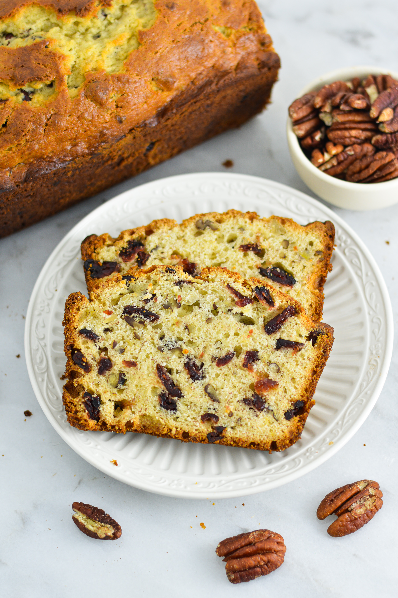 Two slices of Cranberry Pecan Banana Bread with pecans in the background.