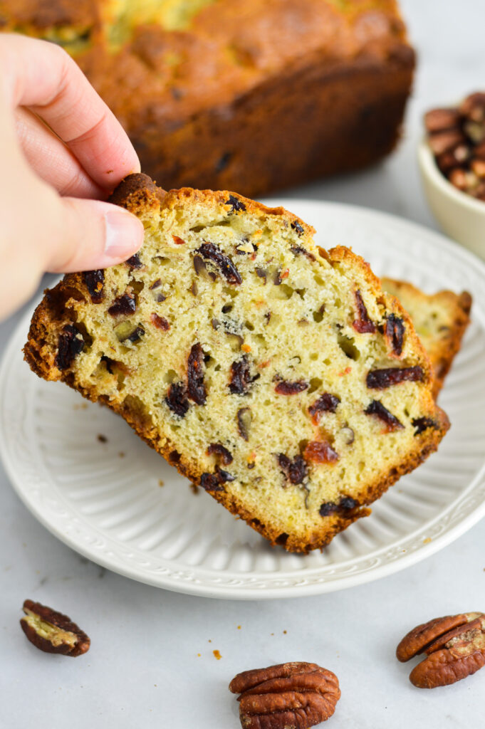 A hand taking a slice of Cranberry Pecan Banana Bread.