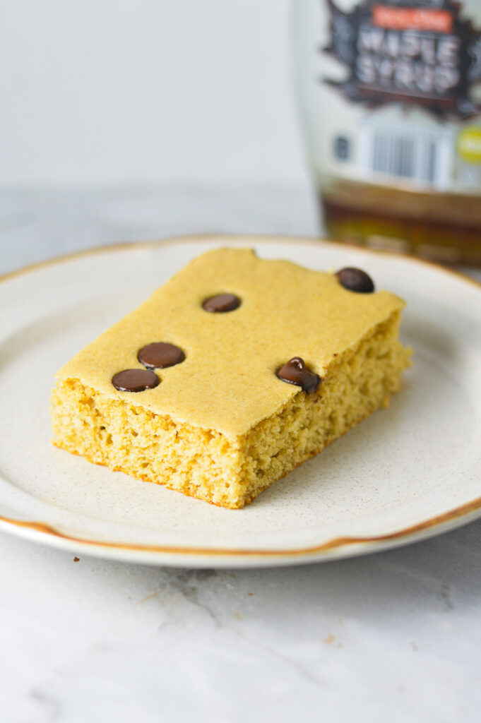 An Easy Chocolate Chip Sheet Pan Pancake on a dessert plate with a jar of maple syrup in the background.