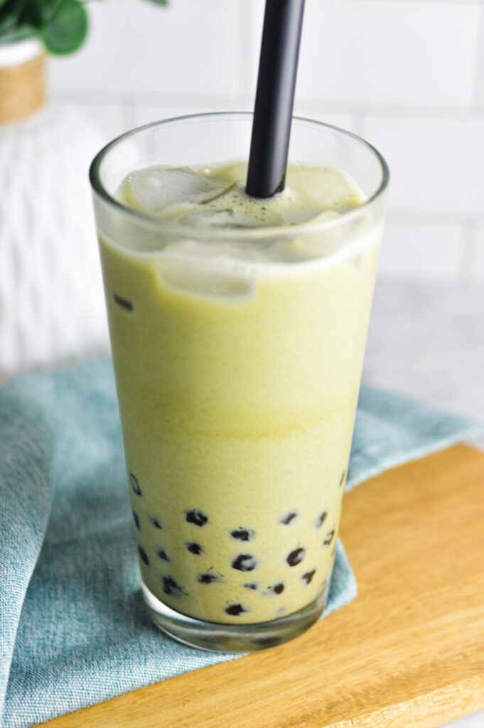 A cold Iced Matcha Bubble Tea drink in a tall glass. A matte black straw is sticking in the creamy green matcha drink.