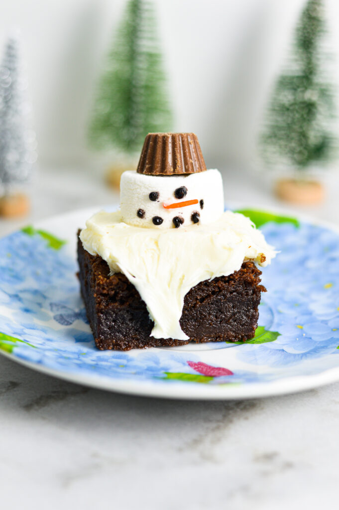 Melted Snowman Nutella Brownies with white frosting on top of a fudgy Nutella brownie. A small peanut butter cup is used for the marshmallow snowman's hat.