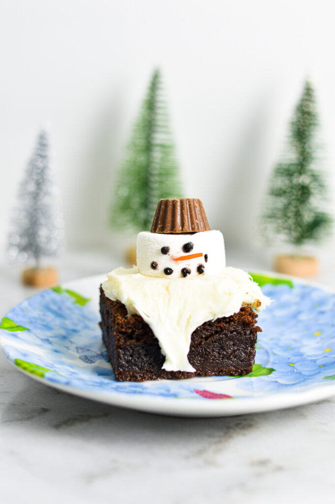 A Melted Snowman Nutella Brownie with a mini Reese's cup for a hat. Small pine tree decorations are in the background giving it a Christmastime feeling.