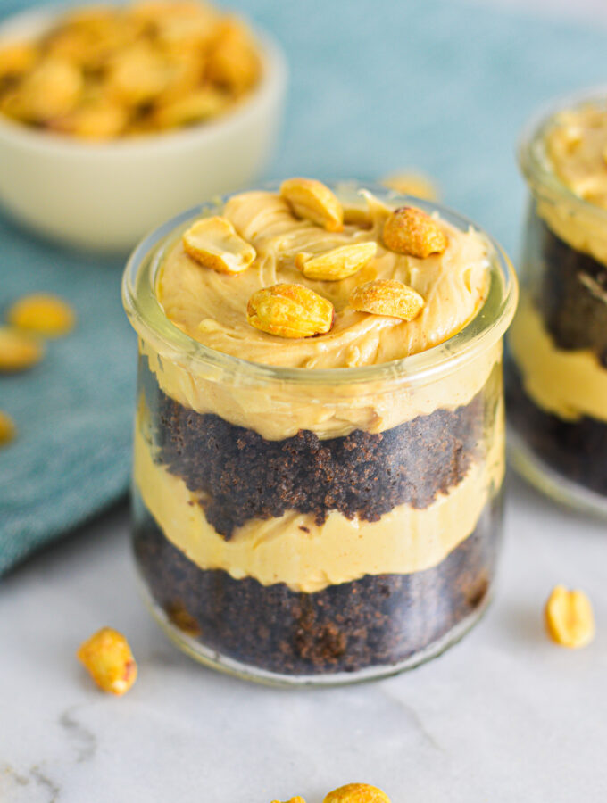 Rich Peanut Butter Chocolate Cake Cheesecake Cups in small glass containers. Layers of creamy cheesecake and rich chocolate cake all topped with crunchy peanuts.