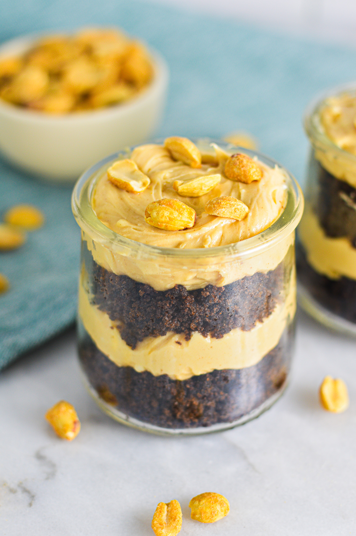 Rich Peanut Butter Chocolate Cake Cheesecake Cups in small glass containers. Layers of creamy cheesecake and rich chocolate cake all topped with crunchy peanuts.