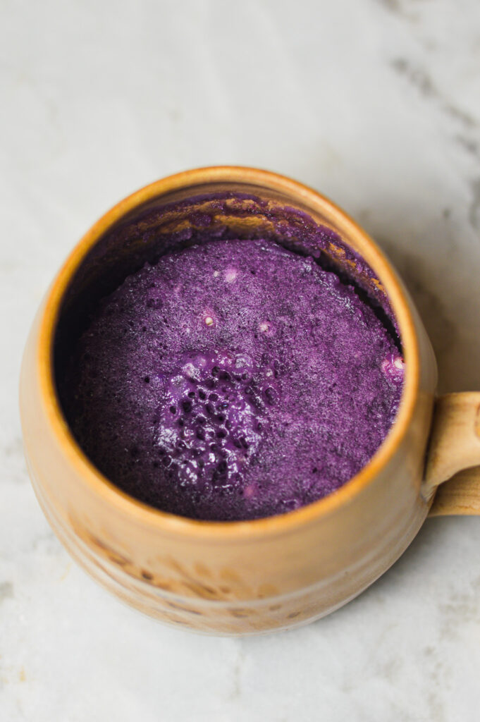 A beige ceramic coffee mug with a bright purple Taro Mug Cake in it.