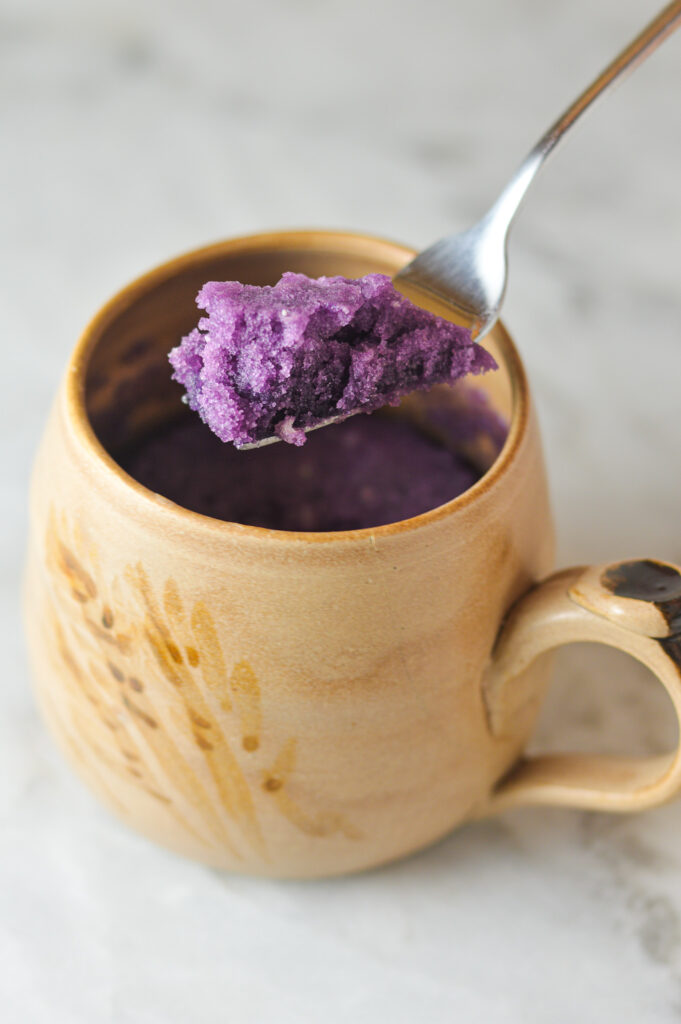 A forkful of rich purple Taro Mug Cake coming out of a large coffee mug. 