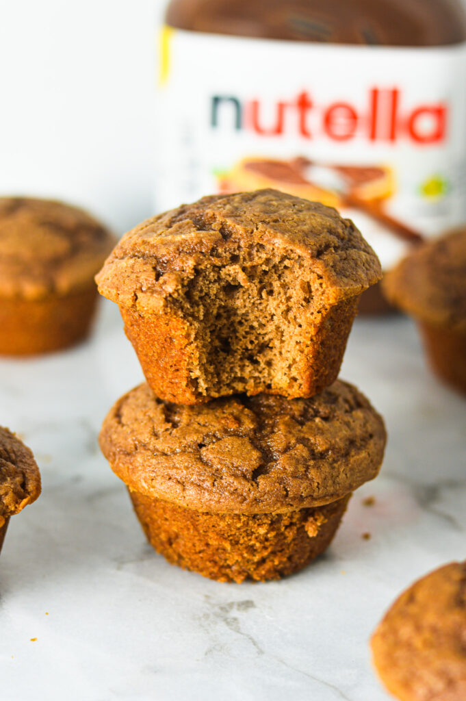 A stack of Yogurt Nutella Muffins with a bite taken out of the top muffin showing a soft and fluffy interior.