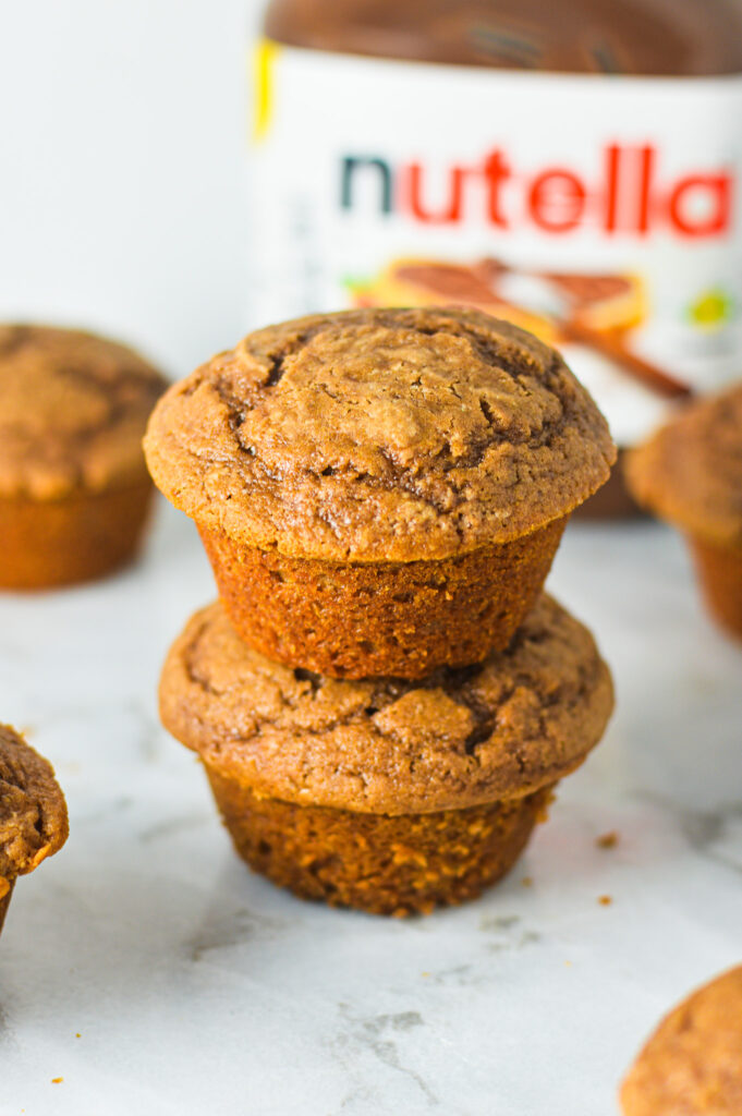 A stack of fluffy Yogurt Nutella Muffins with a jar of Nutella in the background.