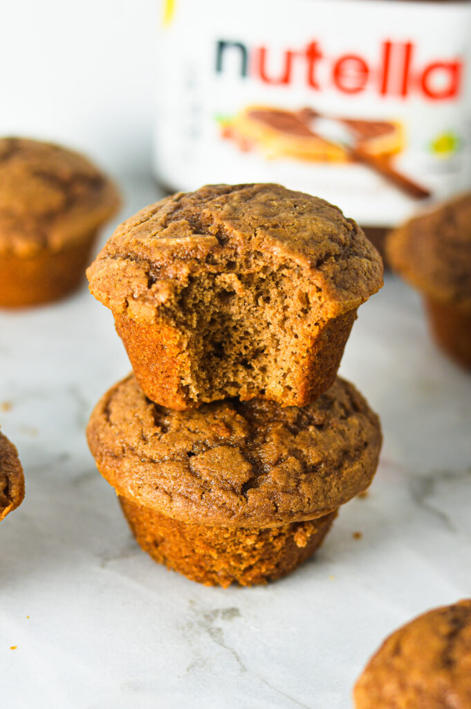 Yogurt Nutella Muffins with crackled tops and a bite taken out of a muffin showing the light and moist interior.