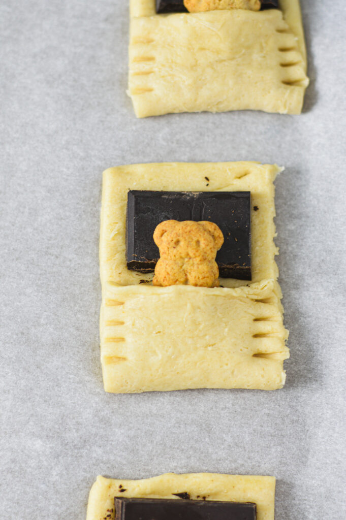 An uncooked Bear in a Blanket, with deep fork marks pressing the pale crescent dough shut.