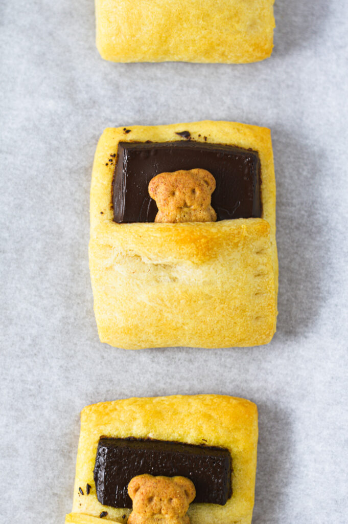 A parchment paper lined baking sheet with teddy graham Bears in a Blanket.