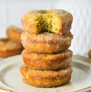 A small plate with a stack of Cinnamon Sugar Banana Bread Donuts. The top donut has a bite taken out of it revealing a fluffy cakelike texture.