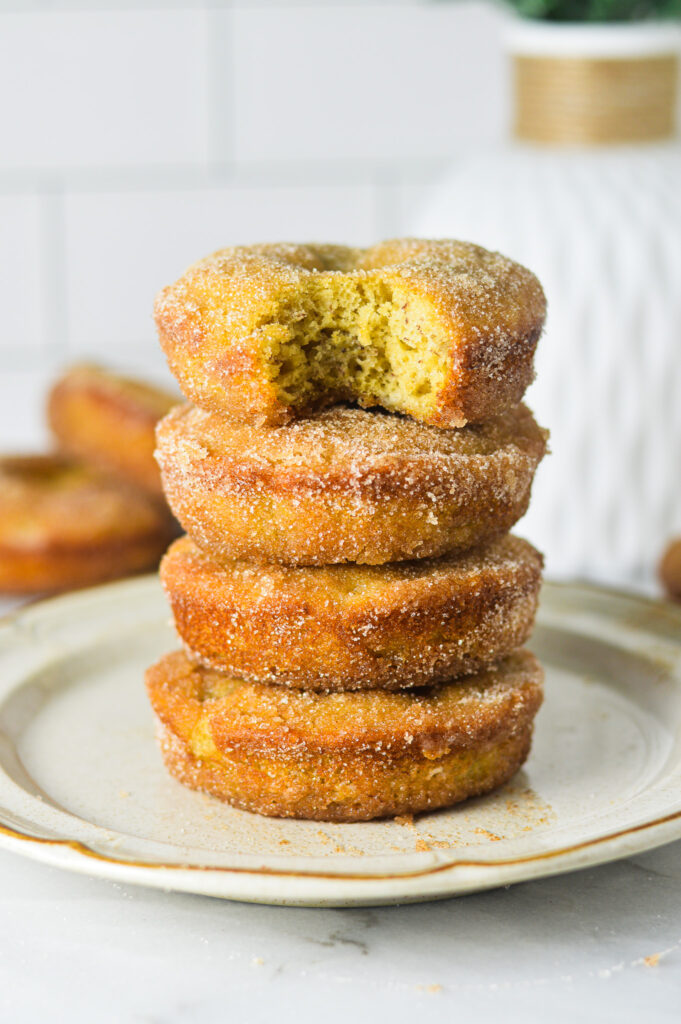 A small plate with a stack of Cinnamon Sugar Banana Bread Donuts. The top donut has a bite taken out of it revealing a fluffy cakelike texture.