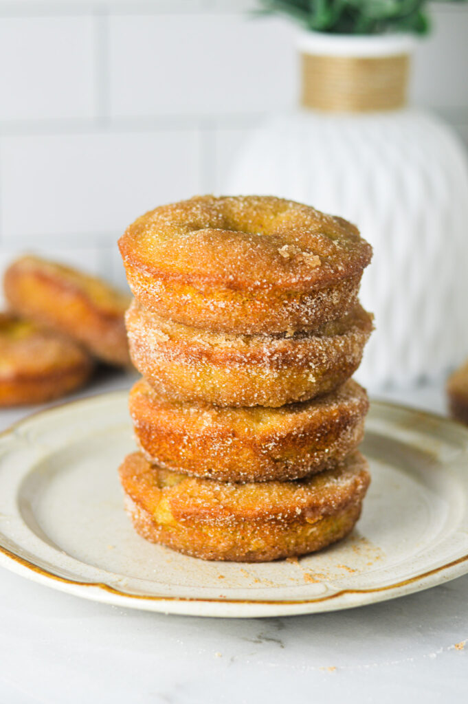 A stack of Cinnamon Sugar Banana Bread Donut on a small beige plate. The cinnamon sugar coating creates a crisp looking texture.