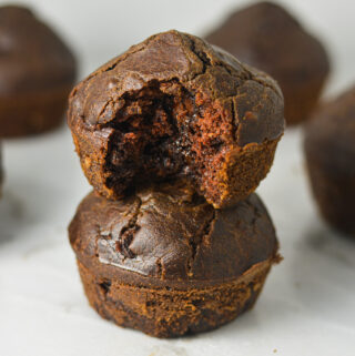 A stack of Healthy Mocha Muffins with a bite taken out of the top muffin revealing a rich chocolate center.