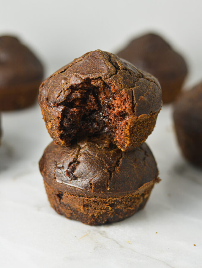 A stack of Healthy Mocha Muffins with a bite taken out of the top muffin revealing a rich chocolate center.