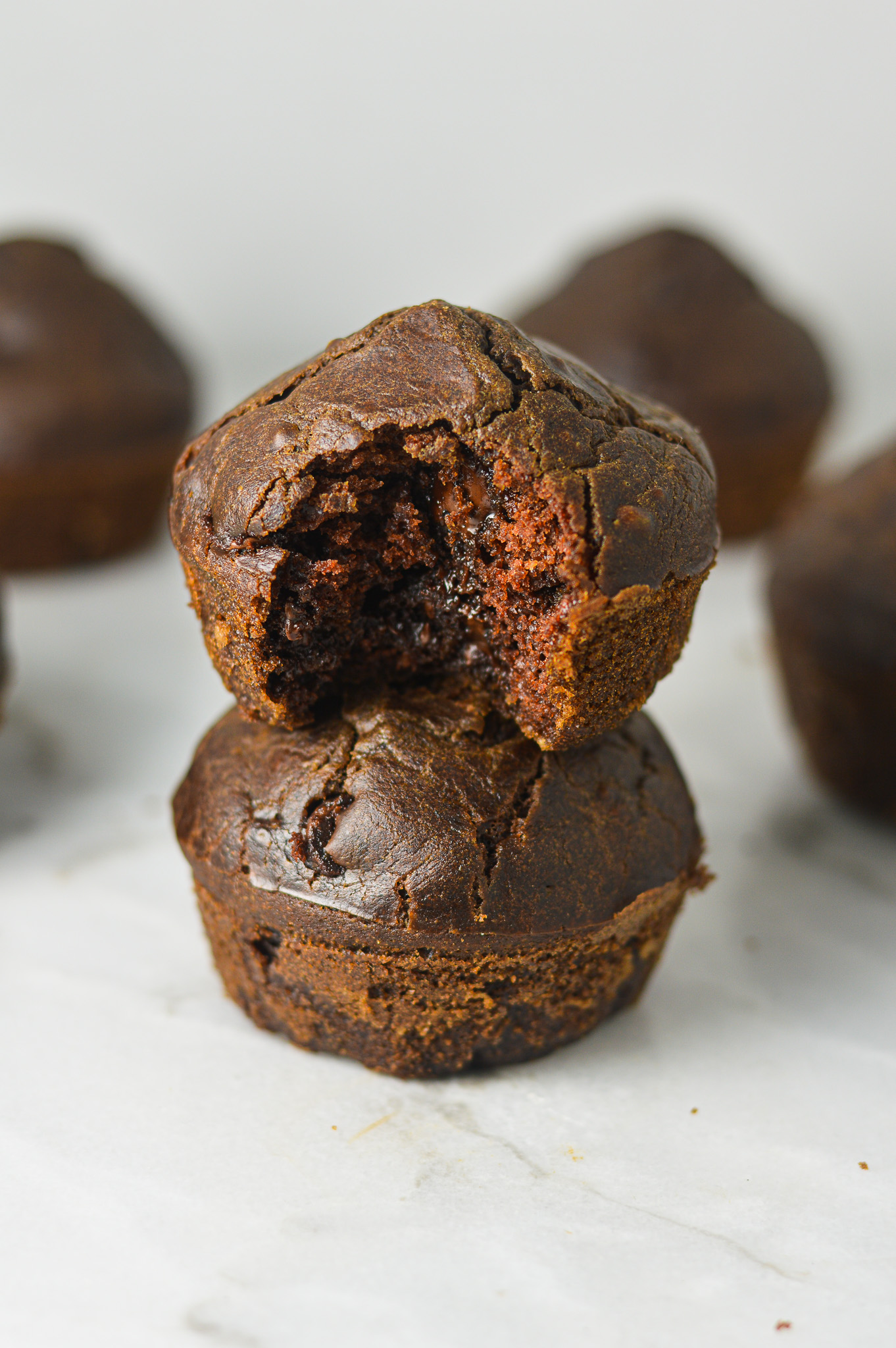 A stack of Healthy Mocha Muffins with a bite taken out of the top muffin revealing a rich chocolate center.