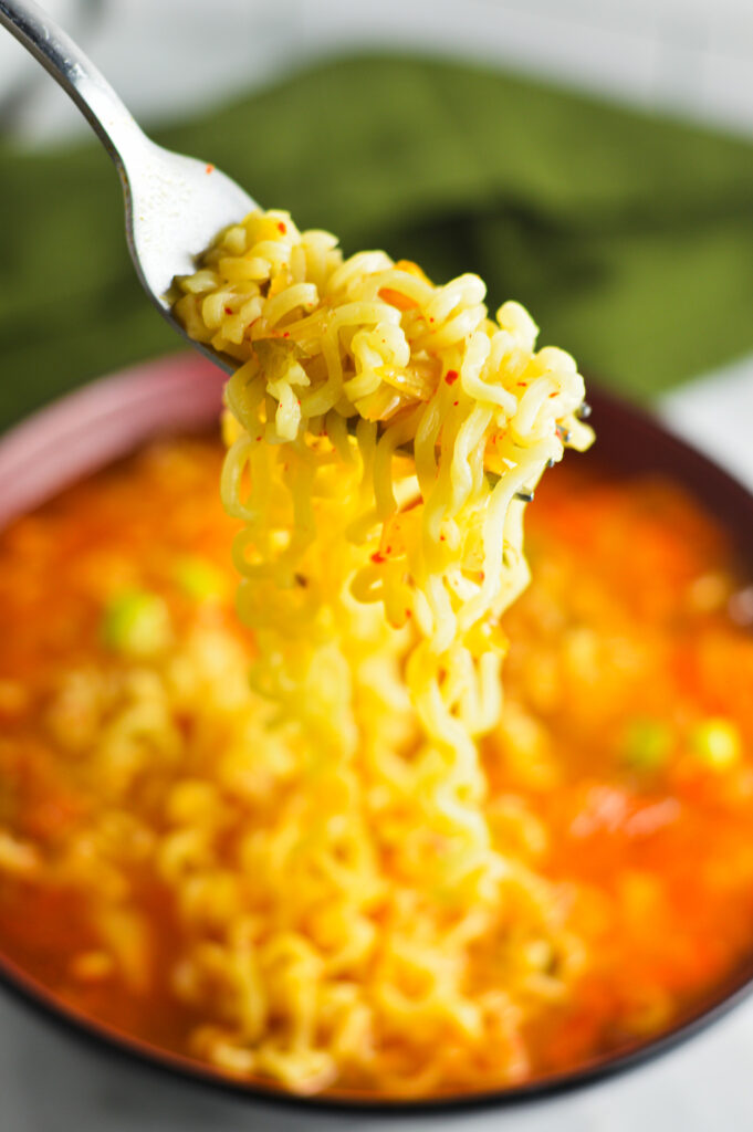 A fork scooping out some noodles out of a steaming hot bowl of Kimchi Ramen.