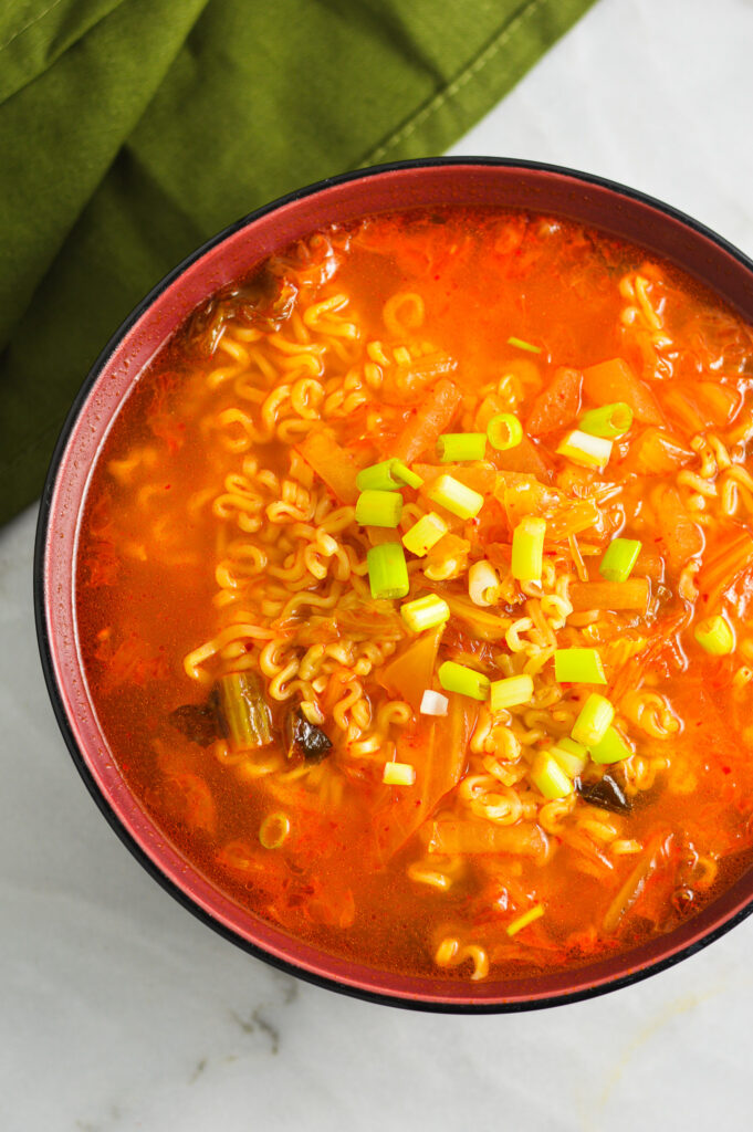 A closeup of a bowl or spicy Kimchi Ramen topped with chopped green onions.