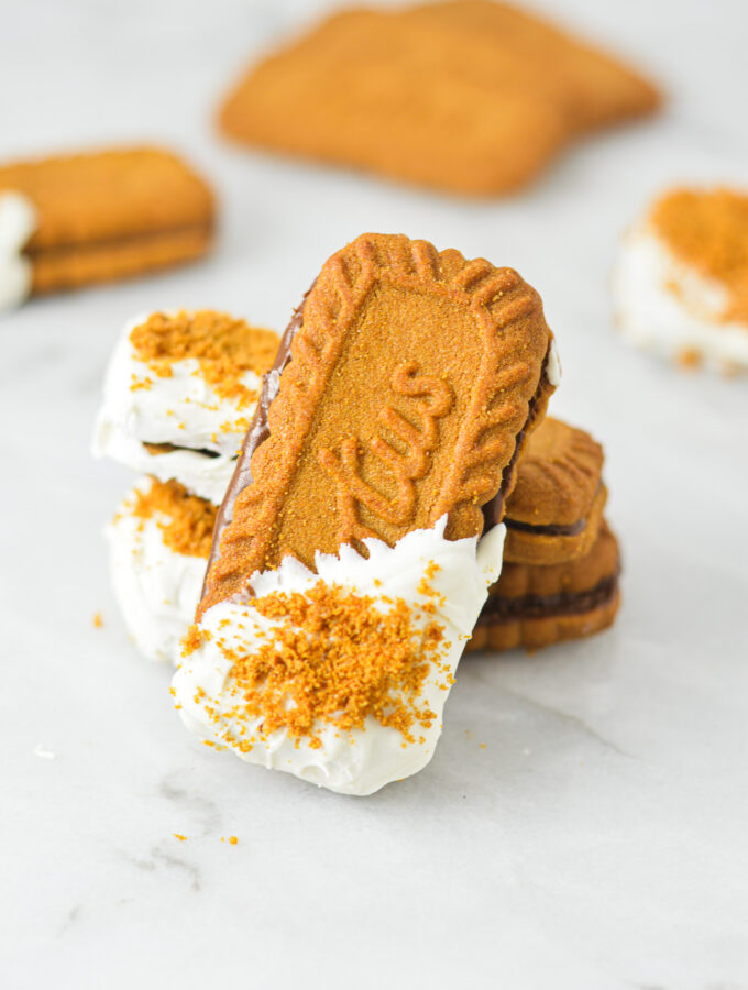 Nutella Biscoff Sandwiches on a granite surface. The Lotus Biscoff Cookie sandwiches are dipped in white chocolate and sprinkled with crushed biscoff cookies.