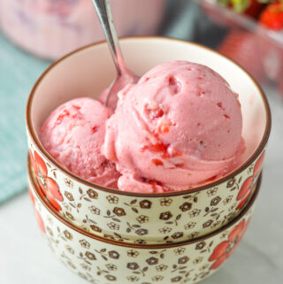 A bowl with some bright pink 3 Ingredient Ninja Creami Strawberry Ice Cream. A spoon is in the bowl, with some strawberry pieces peeking out of the creamy ice cream.