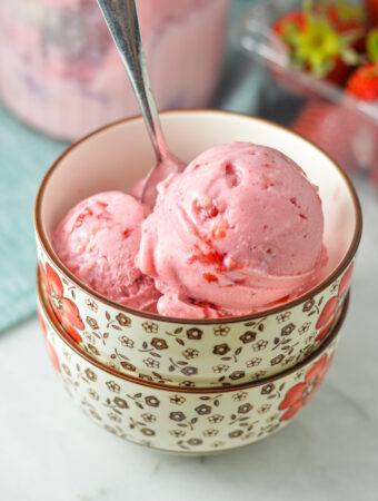 A bowl with some bright pink 3 Ingredient Ninja Creami Strawberry Ice Cream. A spoon is in the bowl, with some strawberry pieces peeking out of the creamy ice cream.