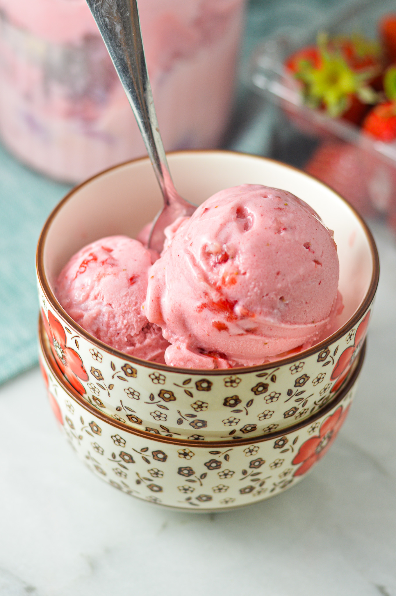 A bowl with some bright pink 3 Ingredient Ninja Creami Strawberry Ice Cream. A spoon is in the bowl, with some strawberry pieces peeking out of the creamy ice cream.