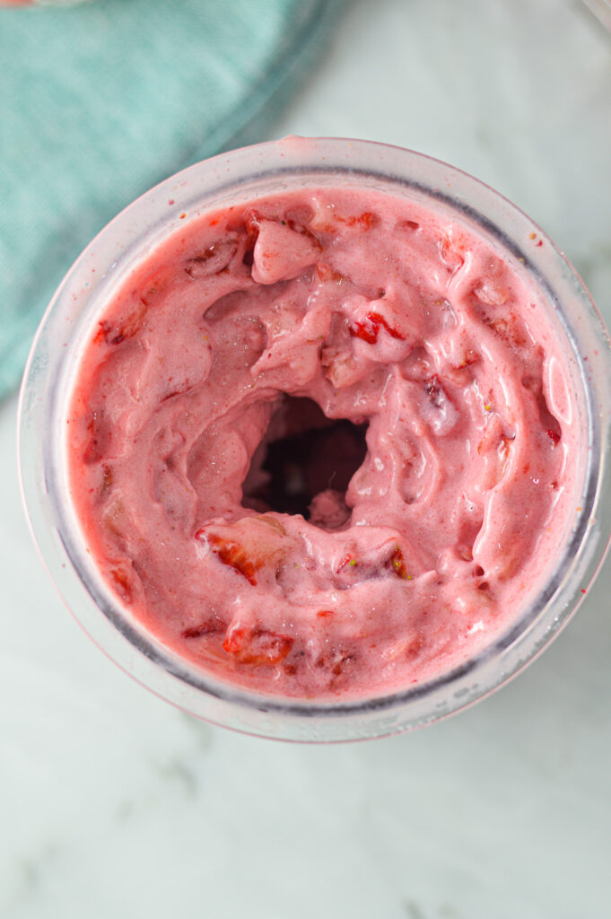 An overhead shot of 3 Ingredient Ninja Creami Strawberry Ice Cream in a Ninja Creami pint, with a hole in the center showing the rich and creamy texture of the dessert.