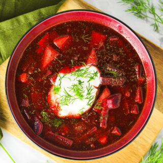 A vibrant red bowl of Instant Pot Borscht with a dollop of sour cream and fresh dill on top.