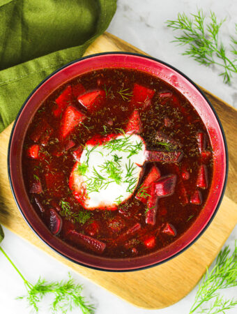 A vibrant red bowl of Instant Pot Borscht with a dollop of sour cream and fresh dill on top.