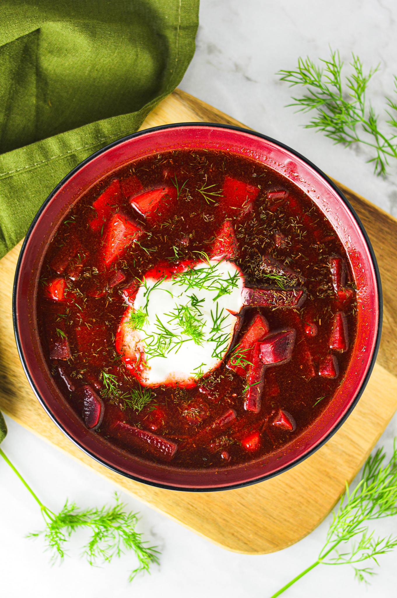 A vibrant red bowl of Instant Pot Borscht with a dollop of sour cream and fresh dill on top.