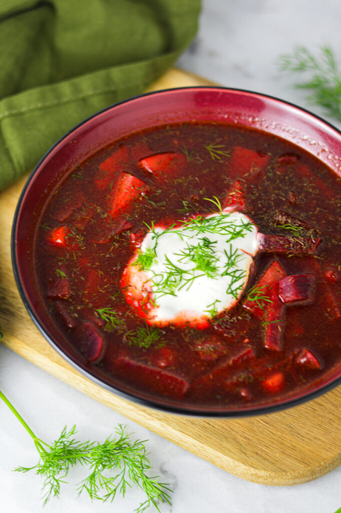 A bowl of dark red Instant Pot Borscht with a scoop of sour cream and fresh dill on top.