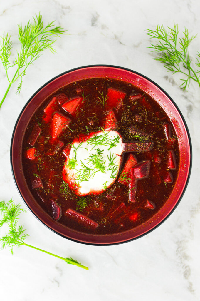 A bowl of vibrant Instant Pot Borscht with a dollop of sour cream and fresh dill on top.