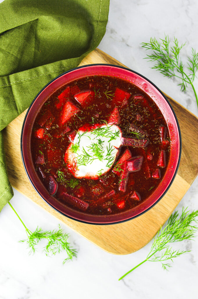 A bowl of homemade Instant Pot Borscht with a scoop of sour cream and fresh dill on top.