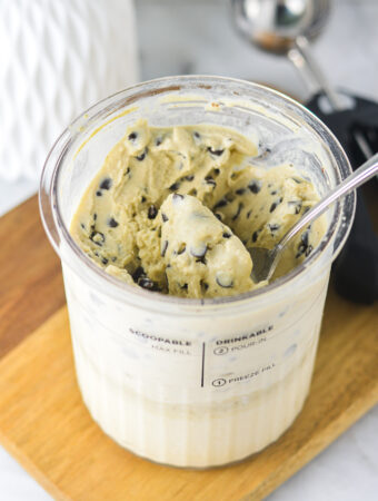 A Ninja Creami pint filled with Ninja Creami Chocolate Chip Protein Ice Cream, with a spoon inside ready to scoop.