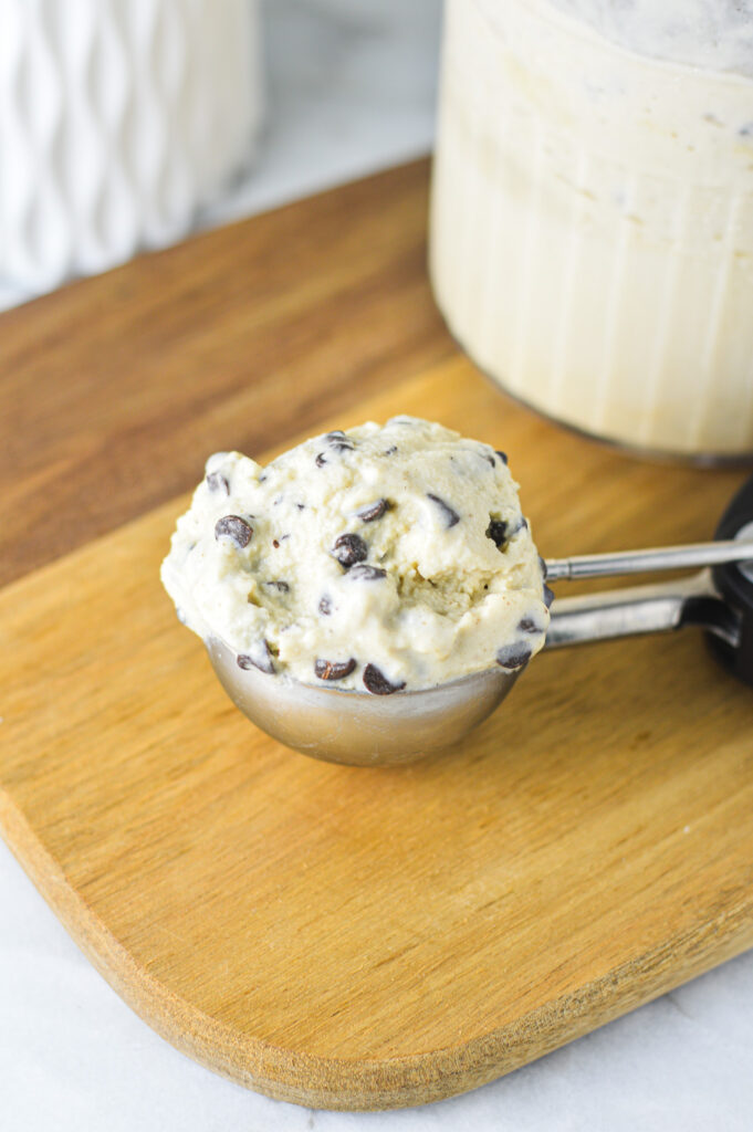 An ice cream scoop with some Ninja Creami Chocolate Chip Protein Ice Cream on a wooden surface.