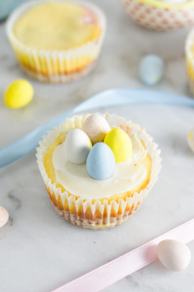 Some Easter Egg Mini Cheesecakes in paper liners, with pastel ribbons giving it a festive feel.